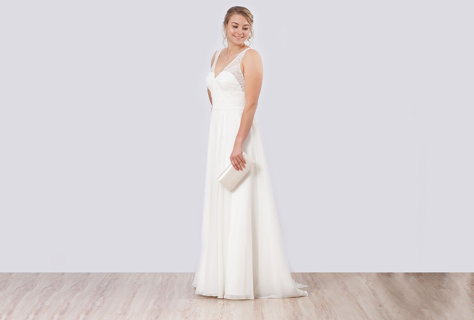 Braut im schlichten Vintage-Brautkleid mit V-Ausschnitt und Perlenstickerei, Clutch in der Hand